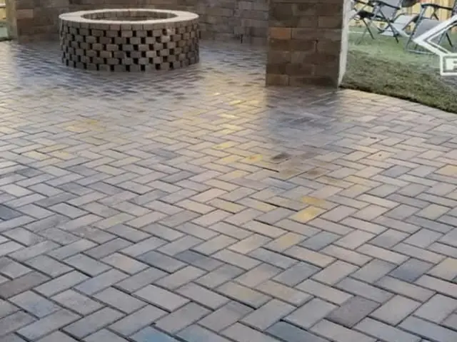A wet paver patio in herringbone with a round fire pit built in a basketweave of the same units, a capped seating wall behind it and two square columns at its ends