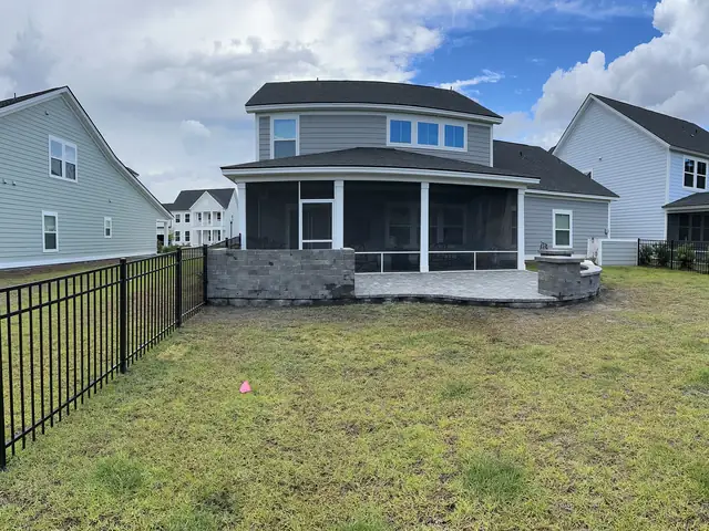The back of a house with a screened porch, a black aluminum fence across the yard and a low gray block counter with a grill built along the porch edge