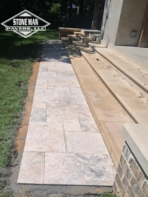 A walkway of large cream stone slabs running alongside a flight of broad cast steps, with a stone-faced knee wall capped in the same cream stone